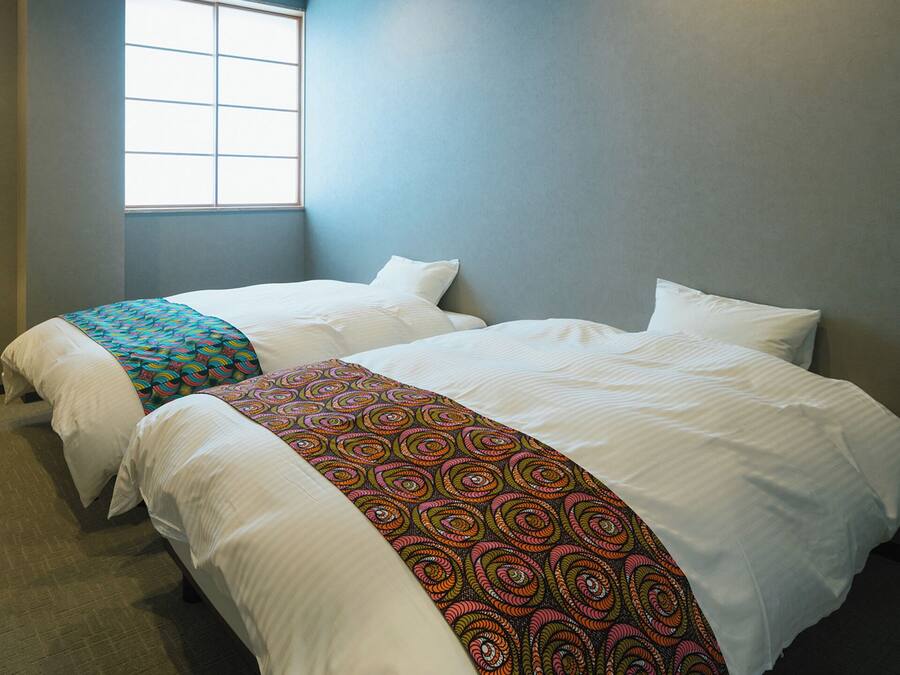 A hotel room with two beds, a floor lamp, and a window.