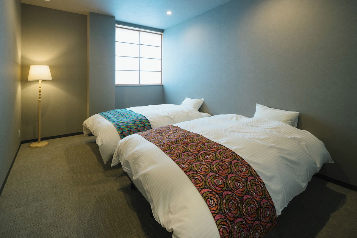 A hotel room with two beds, a standing lamp, and a window.