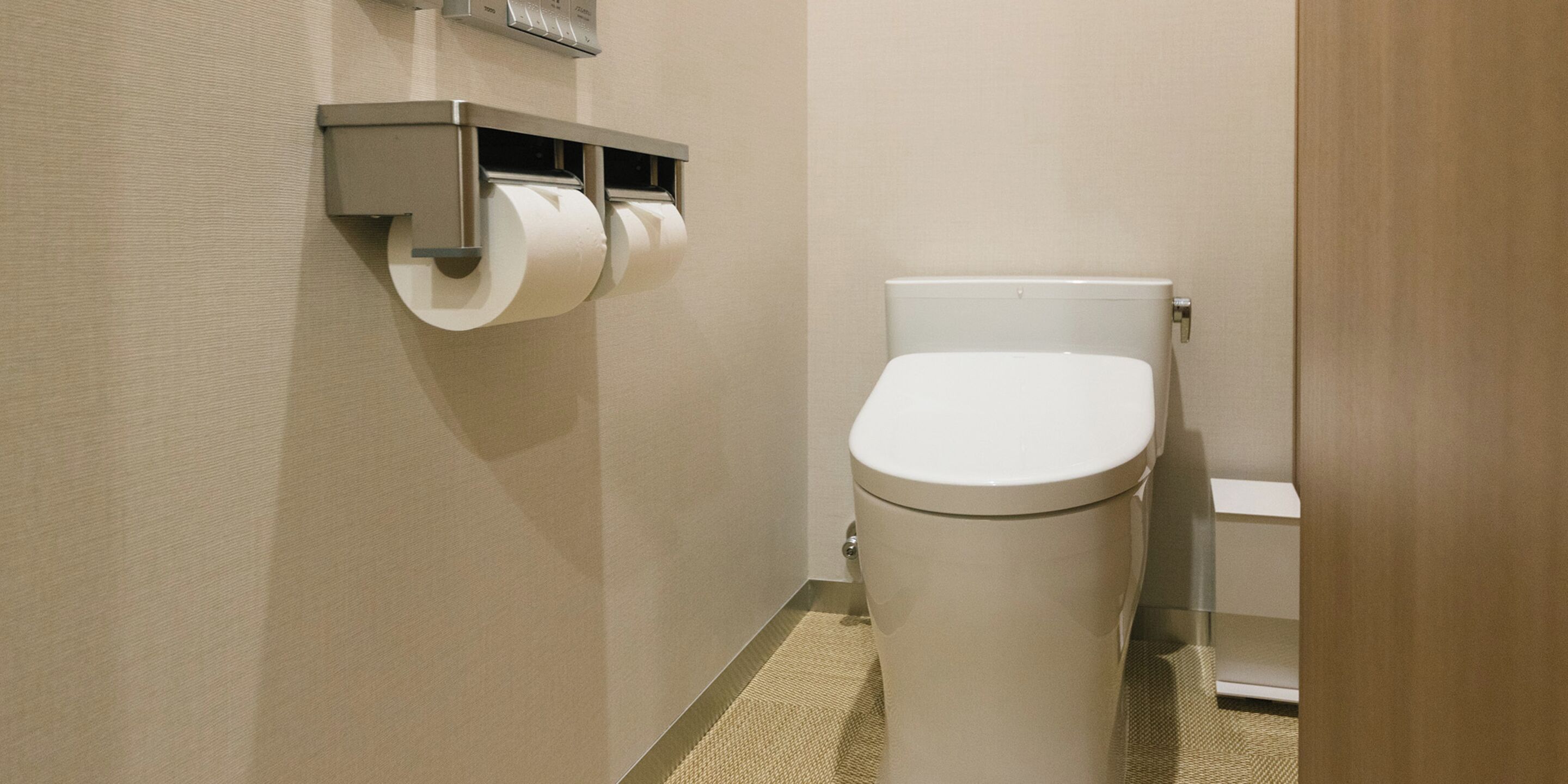 A bathroom with a toilet, a paper towel dispenser, and a toilet paper roll.