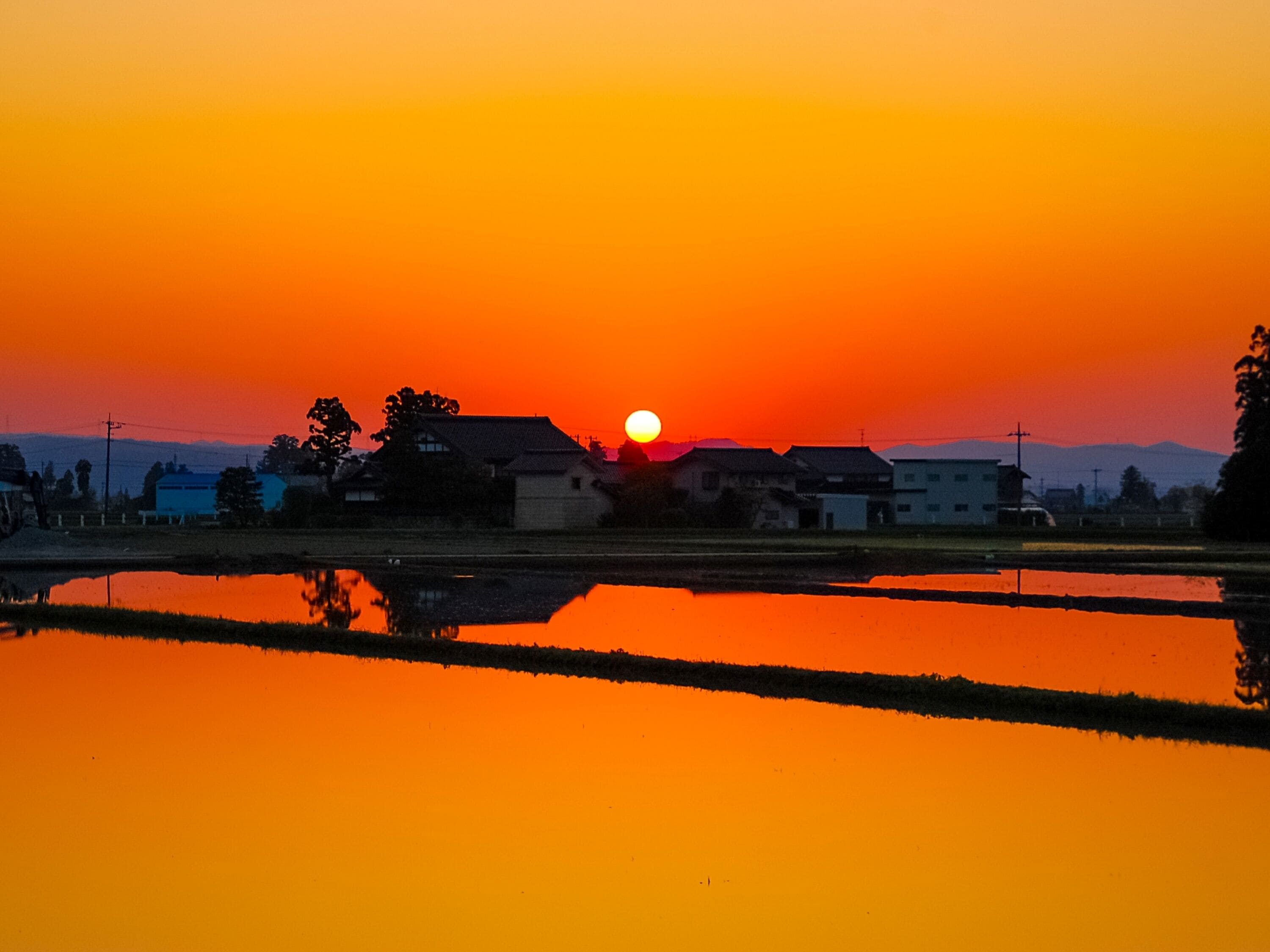 A sunset over a rural landscape with houses and a body of water reflecting the sky.