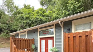 A wooden deck leading to a building with a red door, surrounded by trees.