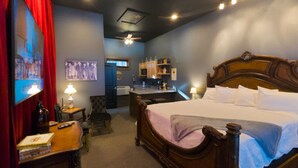 A hotel room with a large bed, a desk, a chair, and a small kitchenette.