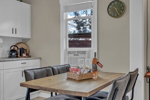 Un coin repas avec une table en bois, des chaises, une horloge et une fenêtre donnant sur des arbres.