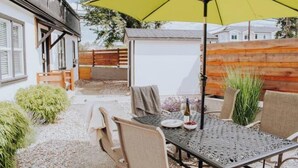 Eine Terrasse im Freien mit Tisch und Stühlen, einem gelben Sonnenschirm und einem kleinen Gartenbereich.