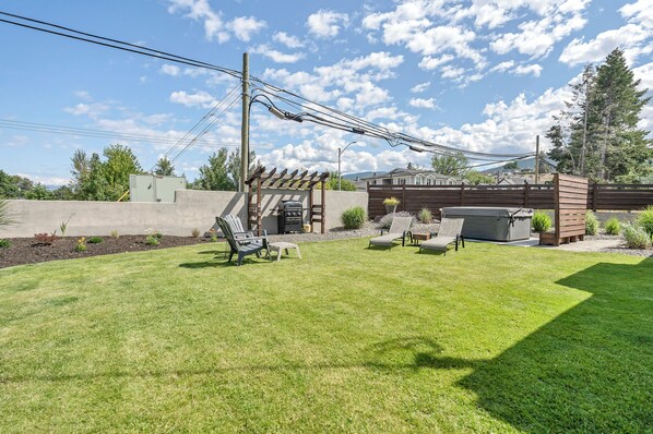 Un patio trasero con una parrilla, muebles de exterior y una pérgola.