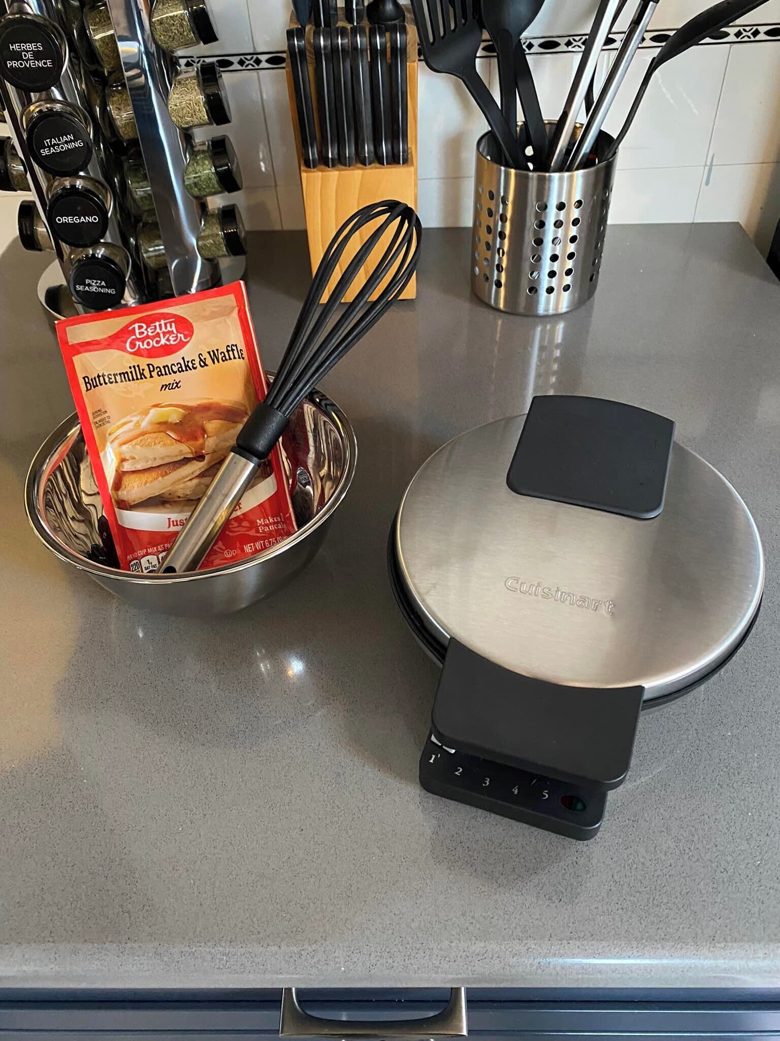 A kitchen counter with a food processor, a packet of Betty Crocker Buttermilk Pancake & Waffle mix, and various kitchen utensils.
