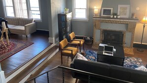 Una sala de estar con chimenea, un sofá, una mesa de comedor con sillas y una estantería.