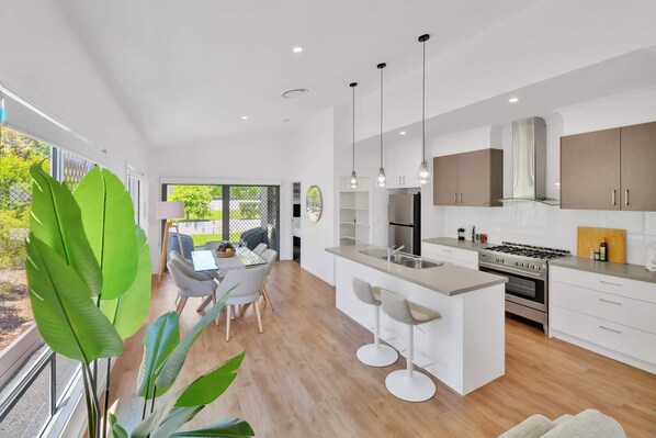 A modern kitchen with white cabinetry, a central island with bar stools, a stainless steel sink, and a gas stove.