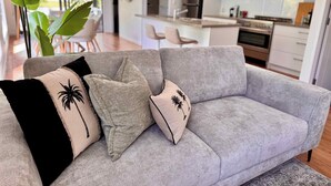 Un soggiorno moderno con un divano grigio, cuscini decorati e una grande pianta verde.