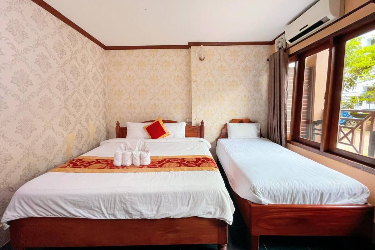 Een hotelkamer met twee houten bedden, een rood-wit gestreepte spreideken en een raam met uitzicht.