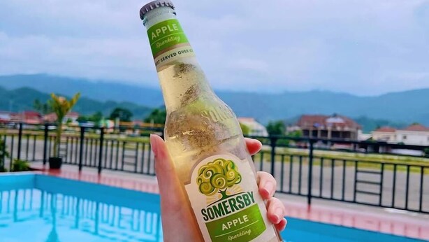 A hand holding a bottle of Somersby Apple Sparkling with a pool in the background. - Vangvieng Sisavang Hotel (Vang Vieng)