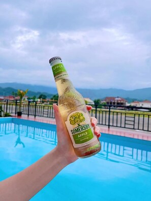 A hand holding a bottle of Somersby Apple Sparkling with a pool in the background. - Vangvieng Sisavang Hotel (Vang Vieng)