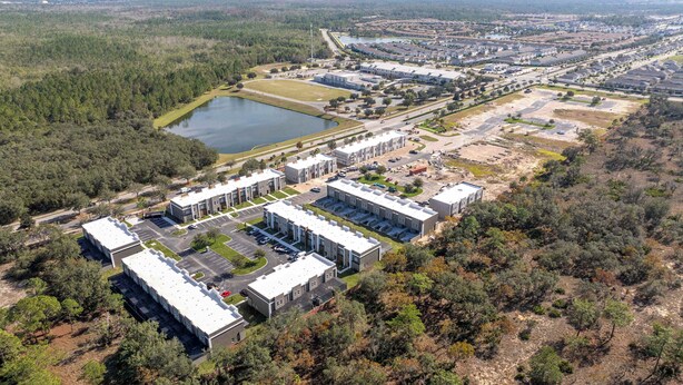 An aerial view of a large industrial complex with multiple buildings, parking areas, and a lake. - New 4BR Villa , themed beds Magic! (Kissimmee)