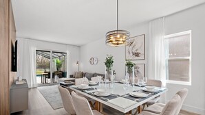 A modern dining area with a glass-top table, beige chairs, and a hanging light fixture. - Brand-New Stylish Home with themed Rooms (Kissimmee)