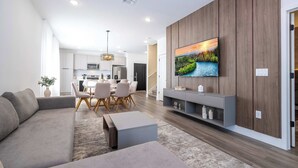 A modern living room with a large flat-screen TV, a sofa, a coffee table, and a dining area with chairs and a table. - Perfect Family Getaway, 4BR & Themed Magic (Kissimmee)