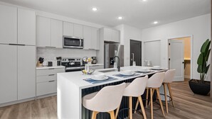 A modern kitchen with white cabinetry, a central island with bar stools, a microwave, a refrigerator, and a sink. - Private Pool Home Near Disney & Themed Rooms (Kissimmee)