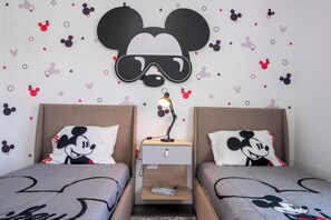 Una habitación con dos camas, cada una con almohadas de Mickey Mouse, un encabezado de Mickey montado en la pared y una mesita de noche con una lámpara.