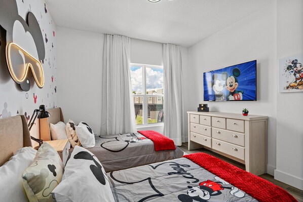 Ein Schlafzimmer mit zwei Betten, einem Fernseher, einem Schminktisch und einem Fenster mit Blick auf Gebäude.