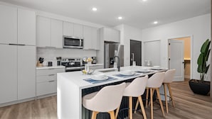 A modern kitchen with white cabinetry, a central island with bar stools, a microwave, a refrigerator, and a sink. - Doppio Luxury Home, Themed Magic! (Kissimmee)