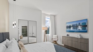 Ein modernes Hotelzimmer mit einem großen Bett, einem Fernseher, einem Kleiderschrank und Blick auf die Stadt.