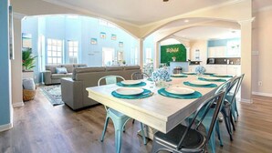 A spacious living area with a dining table set for six, a kitchen in the background, and a ceiling fan. - Starfish Beachfront Swim-Up with HOT TUB (Surfside Beach)