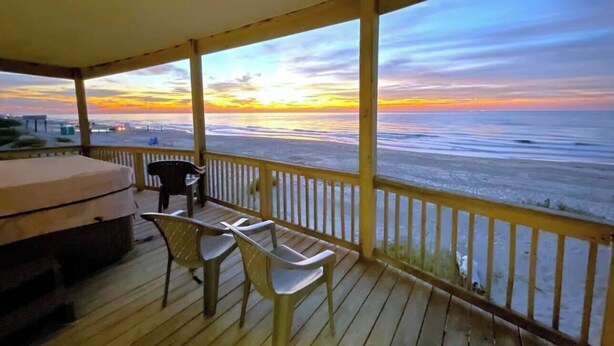 A covered outdoor area with a view of the ocean at sunset, featuring a barbecue grill, two chairs, and a table. - Starfish Beachfront Swim-Up with HOT TUB (Surfside Beach)