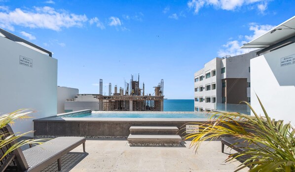 A pool area with a view of the sea, a construction site in the background, and a building with a sign indicating a depth of 4.3 meters. - Avelar: 1BR Near Beach w/ Rooftop Pool & Fast WiFi (Bucerías)