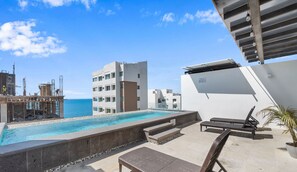 A rooftop pool area with a view of the ocean and a modern building in the background. - Avelar: 1BR Near Beach w/ Rooftop Pool & Fast WiFi (Bucerías)