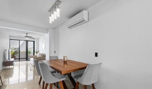 A modern dining area with a wooden table, grey upholstered chairs, and a ceiling fan. - Avelar: 1BR Near Beach w/ Rooftop Pool & Fast WiFi (Bucerías)