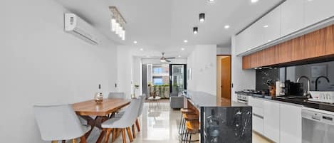 Een moderne keuken met witte kasten, een zwart marmeren eiland en een eetgedeelte met een houten tafel en grijze stoelen.