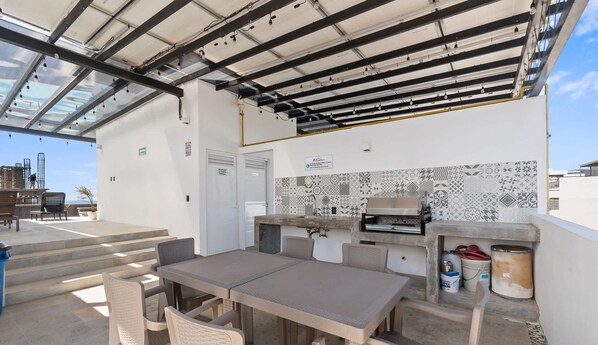 An outdoor patio with a table and chairs, a grill, and a tiled backsplash. - Avelar: 1BR Near Beach w/ Rooftop Pool & Fast WiFi (Bucerías)