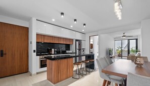 A modern kitchen with a central island, bar stools, and a dining area with a table and chairs. - Avelar: 1BR Near Beach w/ Rooftop Pool & Fast WiFi (Bucerías)
