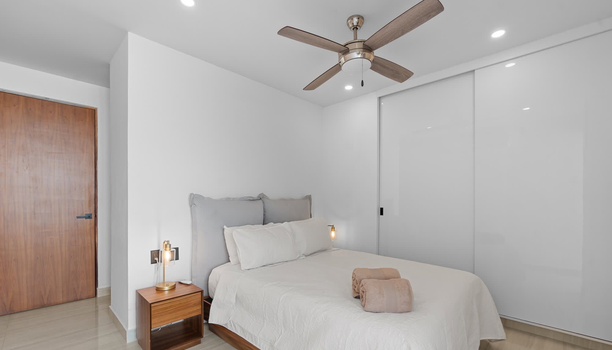 A bedroom with a bed, a nightstand, a ceiling fan, and a wardrobe.