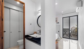 A modern bathroom with a toilet, sink, and mirror. There is a sliding door and a window with a view of the outside.