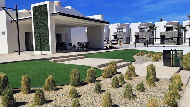 A modern residential complex with white buildings, green artificial grass, and small shrubs. - Charming 2-bedroom apartment in Los Cabos with WiFi, AC, Swimming Pool and more. (B.C.S.)