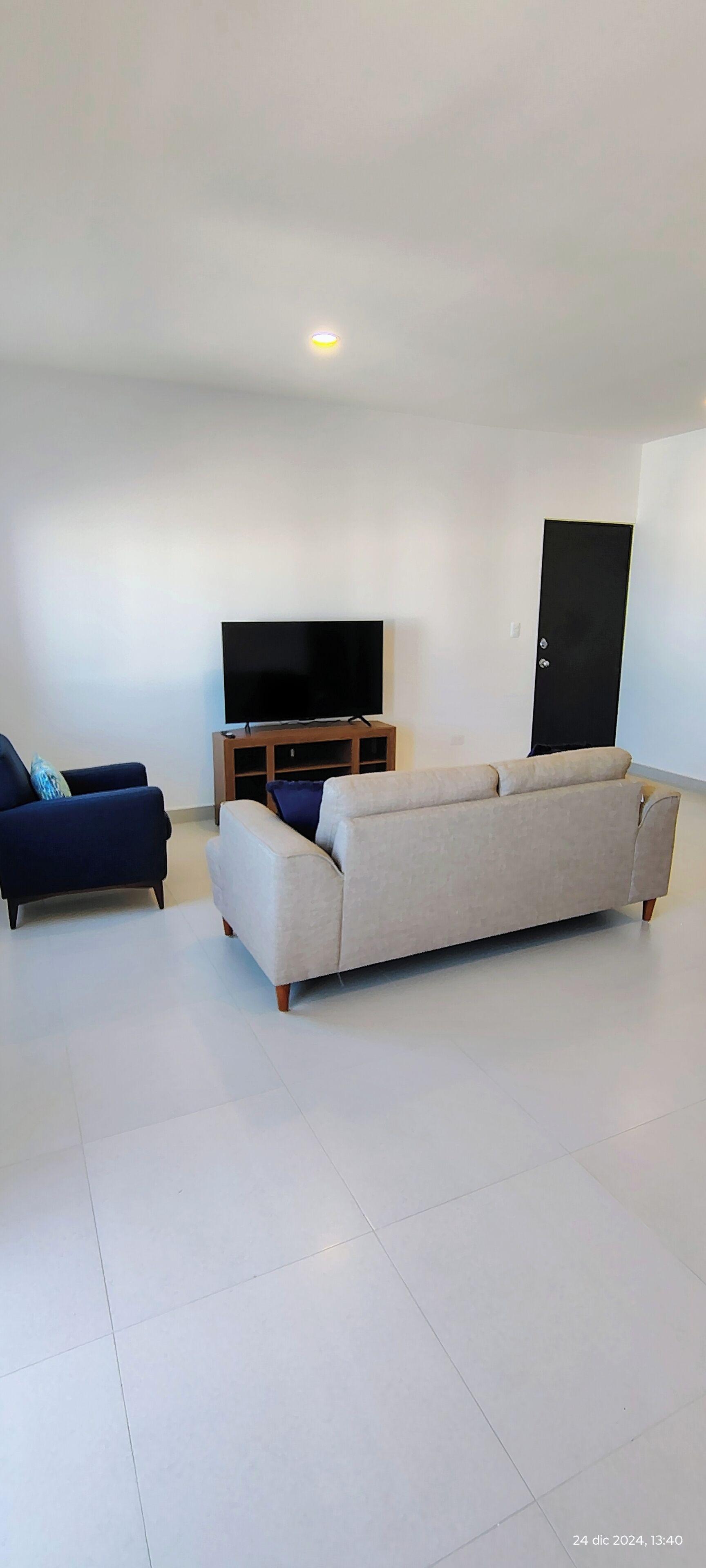 A living room with a sofa, a blue armchair, and a TV on a wooden stand.