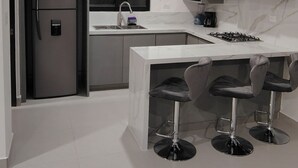A modern kitchen with a built-in refrigerator, a gas stove, and a sink. There are three bar stools under a white countertop. - Charming 2-bedroom apartment in Los Cabos with WiFi, AC, Swimming Pool and more. (B.C.S.)