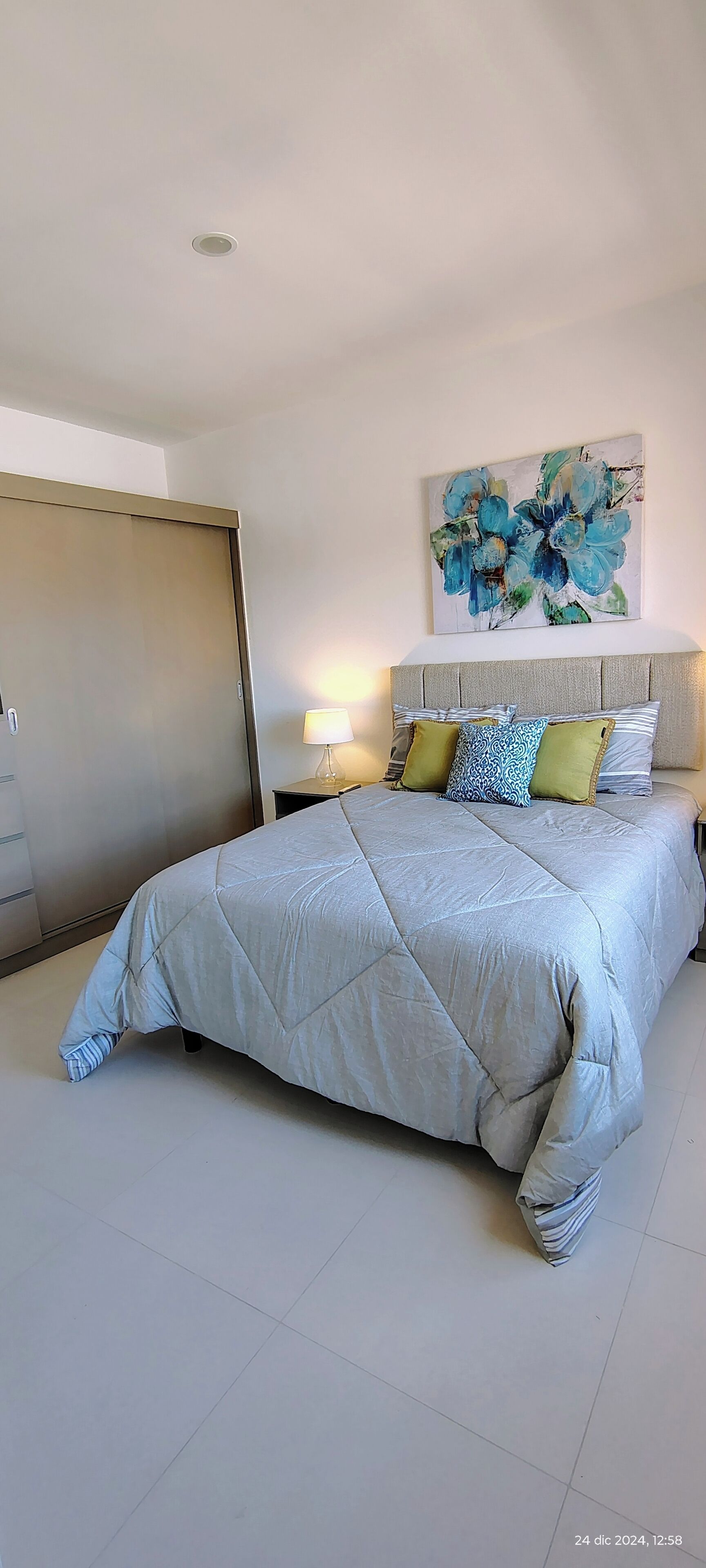 Een slaapkamer met een bed, nachtkastje, lamp, schilderij en garderobe.