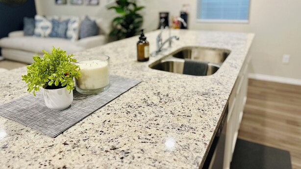 Una cocina con encimera de granito, un lavamanos, una pequeña planta en maceta y una vela.