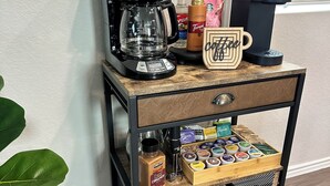 Una estación de café con una cafetera Hamilton Beach, siropes Torani, una máquina Keurig y una taza de madera con la palabra 'Coffee'.