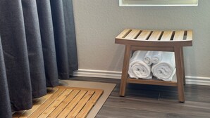 Un taburete de madera con toallas, un felpudo de madera y una ventana con cortinas.