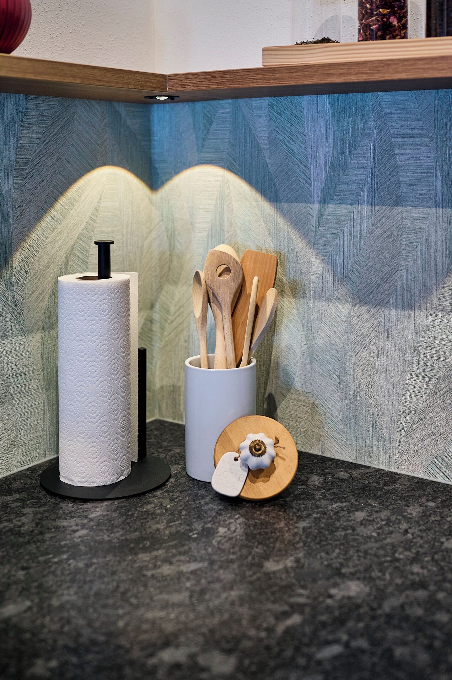 A kitchen counter with a paper towel holder, wooden utensils, and a small decorative item.