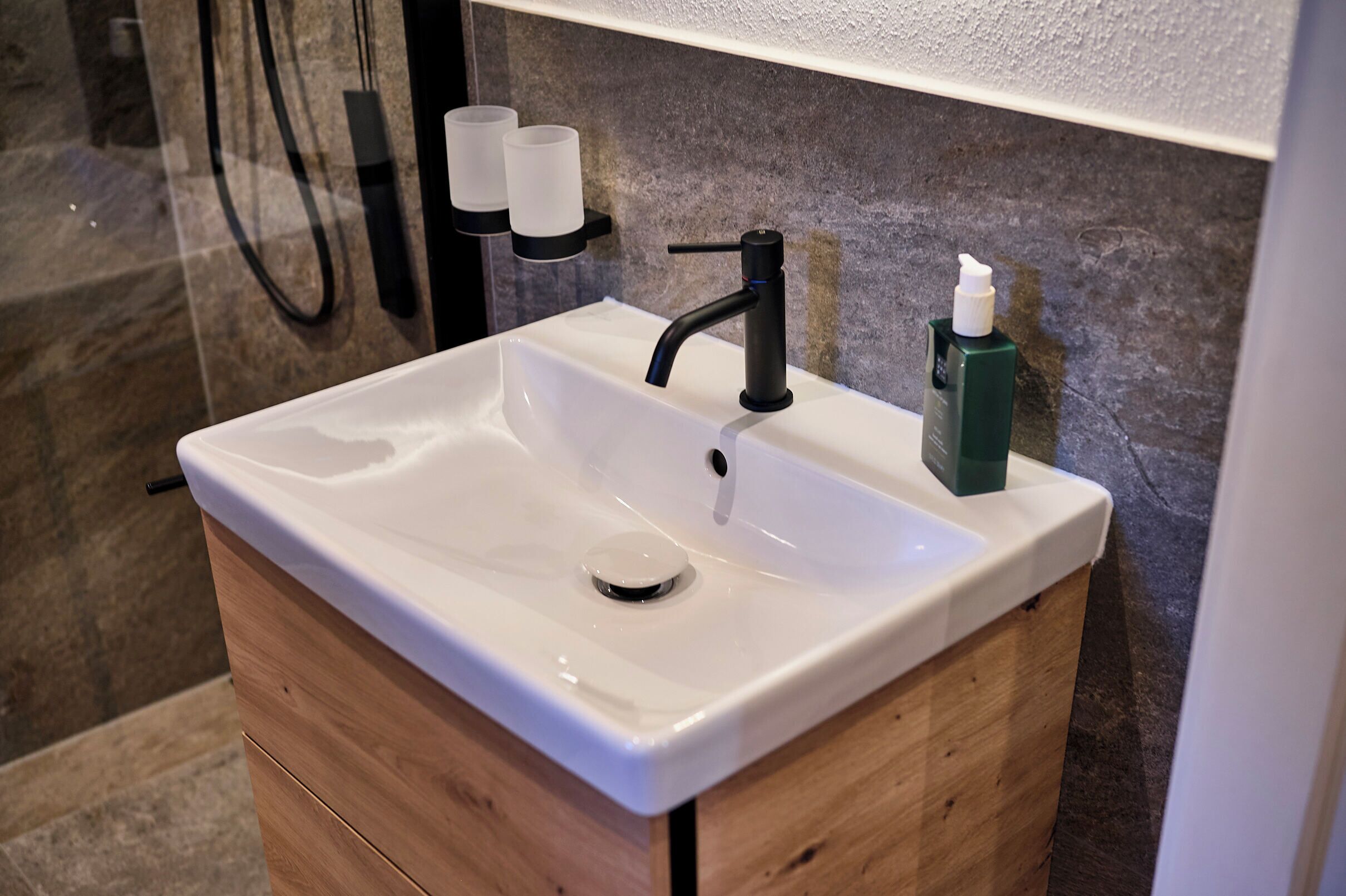 Un bagno con un lavandino bianco, un rubinetto nero e un dispenser di sapone verde.