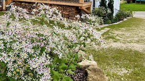Een houten huis met balkon, stenen fundering en een tuin met witte bloemen.