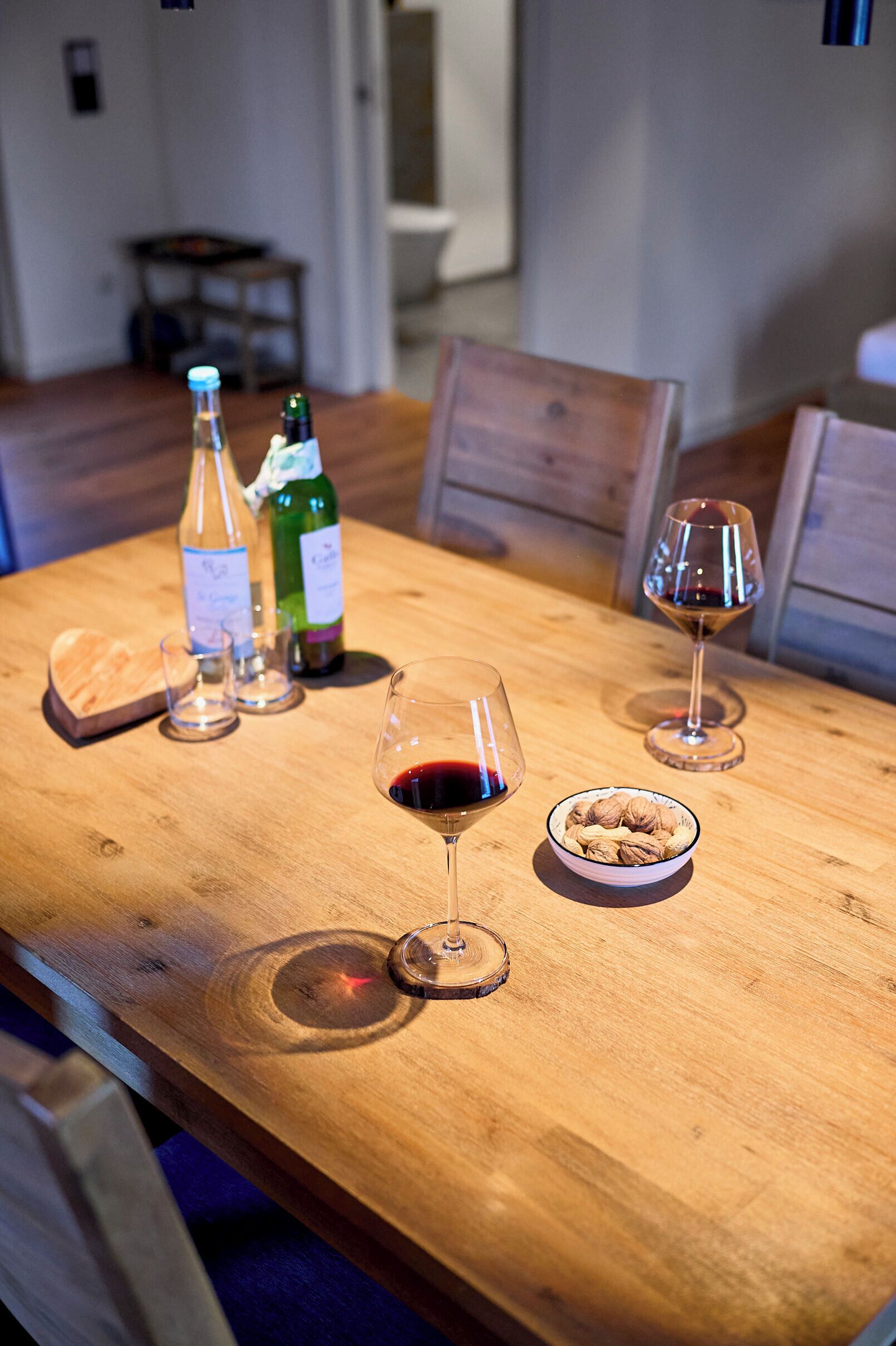 A wooden dining table with wine bottles, glasses, and a bowl of nuts.