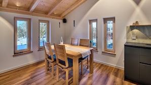 Een eetruimte met een houten tafel en stoelen, grote ramen en een keukenhoek.