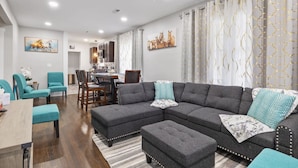 A modern living room with a sectional sofa, ottomans, and teal chairs. - Spacious Bungalow Retreat Near Belle Isle, RVA! (Richmond)