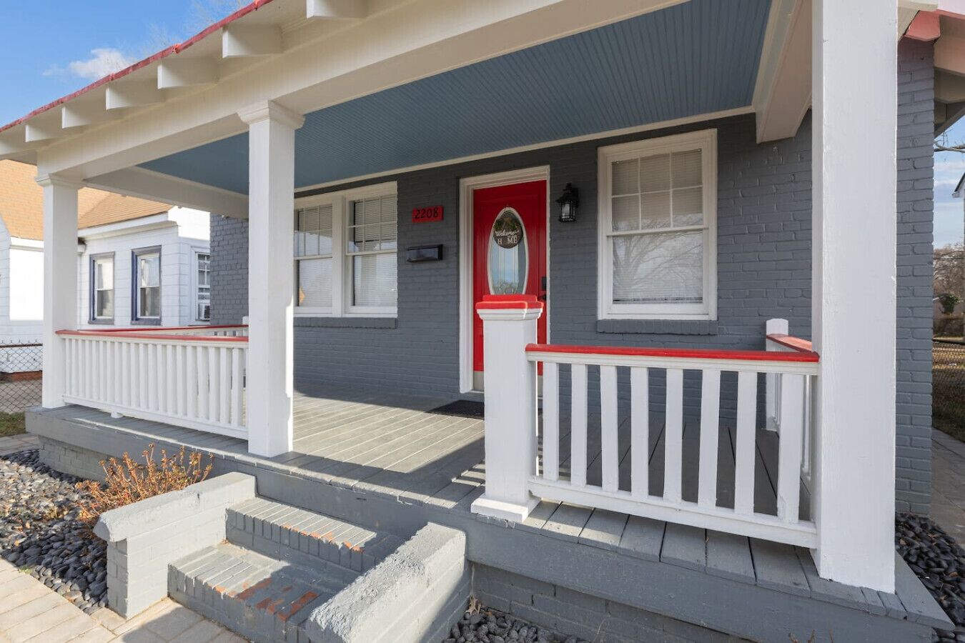 Une maison à deux étages avec une porte d’entrée rouge, des balustrades blanches et une façade grise.