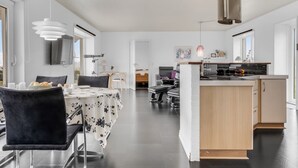 Eine moderne Küche mit Kochinsel, ein Essbereich mit Tisch und Stühlen sowie ein Wohnbereich mit Sofa und Couchtisch.