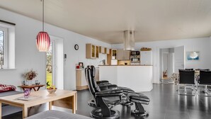 Ein modernes Wohnzimmer mit Essbereich, Küche und einem großen schwarzen Ledersessel.